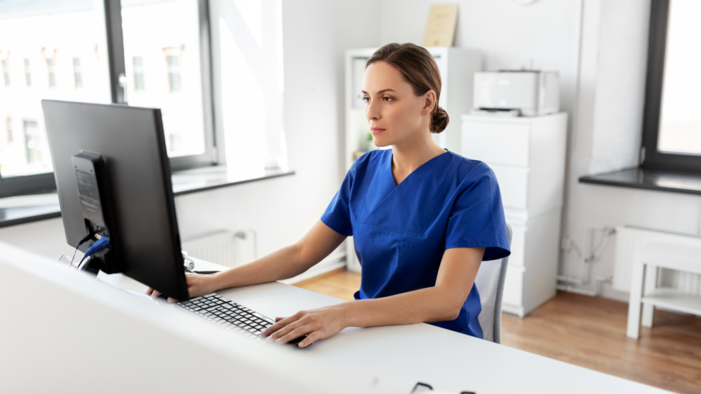 a person in scrubs sitting at a desk in front of a computer